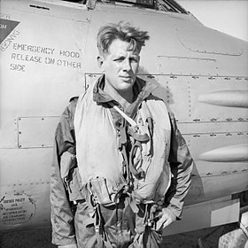 Informal half portrait of blond man in flying gear in front of aircraft