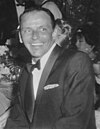 A middle-aged man in a tuxedo sits and smiles into the distance.