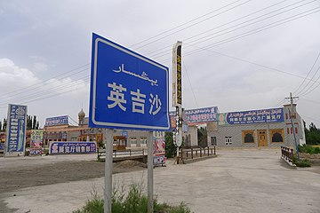 تابلوی ورودی شهر ینگیسار به اویغوری و چینی. در پشت، تابلوی یکی از کارخانه‌های چاقوسازی با نام «انار گولی»، و همین‌طور منارهٔ مسجد کوچکی دیده می‌شوند.