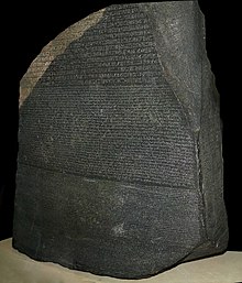 大きく古く黒い石のブロック。1つの面に碑文が書かれている。ところどころが明らかに欠けており、テクストの一部が失われている