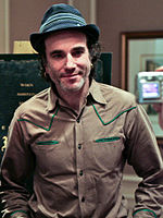Profile of a man wearing a brown and green jacket and a green hat.