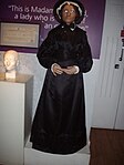 Madame Tussaudová v múzeu v Londýne. Jej posmrtná maska je viditeľná v pozadí vľavo.