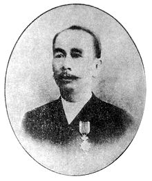Sebuah foto hitam-putih seorang pria Tionghoa mengenakan jas menghadap ke depan