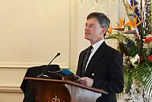 Finlayson speaking at a lectern with flowers behind him