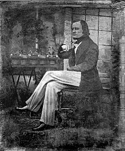 John William Draper, há muito creditado como a primeira pessoa a tirar uma imagem do rosto humano, sentado com seu experimento de plantas, caneta na mão, na NYU no outono de 1839.