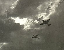 Two Spitfire single-seat piston-engined fighters in flight, silhouetted against cloud