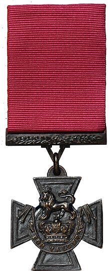a bronze Cross pattée suspended from a crimson ribbon
