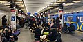 避難者数が膨大で構内だけでは場所が足りないので、プラットホーム上にも避難者が座っている。列車の運行も行われ、乗降客もホームを歩いている（2022年、ウクライナの首都キーウの地下鉄駅にて）。