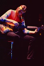 Una fotografia a colori di Jaco Pastorius seduto mentre suona il basso