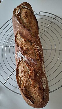 A gold/brown bread on a volette, 3 slits are visible and a bit of flour appears on the surface