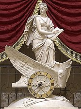 En la mitología griega, Clío era la musa o diosa protectora de la Historia, además de la poesía épica. Aquí aparece observando antes de anotar en su libro, desde un carro alado cuya rueda es la esfera de un reloj.
