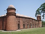Building of red bricks with a roof consisting of many white domes. There are small round towers on the corners of the building each crowned by a white cupola.