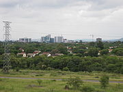 A skyline picture of Gaborone with a field, forest, and low-lying houses in the foreground and buildings along the horizon.