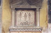 Genius leluhur (tengah atas) diapit oleh Lares, dengan ular di bawah. Lararium, Rumah Vettii Pompeii