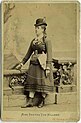 Die Schwarz-Weiß-Fotografie zeigt Bertha von Hillern in Vollperspektive. Sie steht leicht seitlich an einer Ballustrade und trägt einen Hut, ein dunkles, unterschenkellanges Kleid und Stiefel.