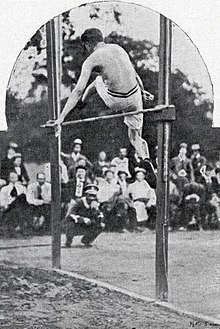 Photo d'un athlète, de dos, qui saut par-dessus une barre.