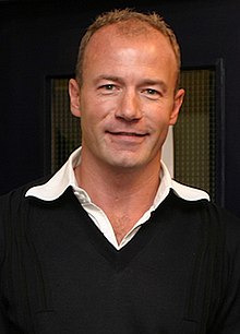 Alan Shearer wearing a black jumper with a white collar visible.
