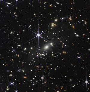 Nền của không gian là màu đen. Hàng nghìn thiên hà xuất hiện trên toàn bức ảnh. Hình dạng và màu sắc của chúng khác nhau. Một số có nhiều sắc thái khác nhau của màu cam, số khác có màu trắng. Hầu hết các ngôi sao có màu xanh lam và đôi khi lớn bằng những thiên hà xa hơn xuất hiện bên cạnh chúng. Một ngôi sao rất sáng ở ngay phía trên và bên trái tâm. Nó có tám gai nhiễu xạ dài, màu xanh lam sáng. Ở hướng khoảng từ 4 giờ đến 6 giờ trên các gai của nó là một số thiên hà rất sáng. Một nhóm ba thiên hà ở giữa và hai thiên hà ở gần hướng 4 giờ. Các thiên hà này là một phần của cụm thiên hà SMACS 0723, chúng đang làm cong hình dạng của các thiên hà được nhìn thấy xung quanh chúng. Các vòng cung dài màu cam xuất hiện ở bên trái và bên phải về phía trung tâm.
