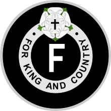 Emblème avec au milieu la lettre F entourée des mots « FOR KING AND COUNTRY » avec au-dessus une rose blanche et une croix de Jésus.