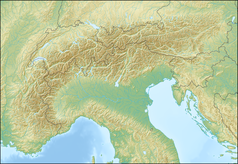 Mapa konturowa Alp, w centrum znajduje się owalna plamka nieco zaostrzona i wystająca na lewo w swoim dolnym rogu z opisem „Lago di Garda”