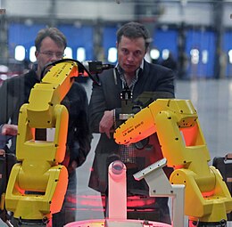 Musk betragter en demonstration af en samlerobot ved genåbningen af NUMMI-fabrikken, nu kaldet Tesla Factory (Fremont, Californien) i 2010