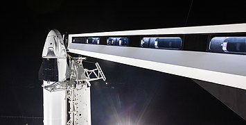Το Dragon 2 πάνω στον Falcon 9, με το βραχίονα προσβάσεις να εκτείνεται από τον πύργο εκτόξευσης έως την κάψουλα.