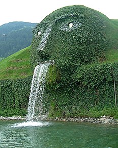 This fountain, flowing out of a green plant-covered head-shaped mound, forms the entrance to the headquarters in Wattens, Austria of Swarovski Crystal.