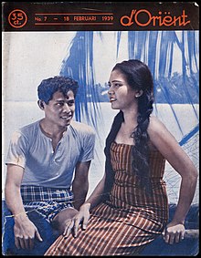 A promotional image showing a woman in a long dress sitting next to a man by the seaside