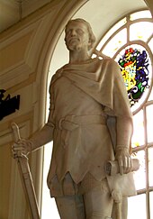 Kip muškarca u tunici i kratkim plaštom na desnom ramenu isklesan u bijelom kamenu. Figura, postavljena u prostoriji leđima okrenuta lučnom prozoru, drži mač okrenut nadolje u desnoj ruci, a svitak u lijevoj.