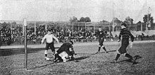 Photo d'un match de rugby, avec trois joueurs debout et deux à terre.