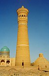 A tall minaret, with domed structures and a blue sky behind.
