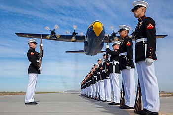 طائرة النقل لوكهيد C-130 هيركوليز التابعة لِفريق الاستعراض الجوي المعروف باسم الملائكة الزرق، تعبر فوق بعض جُنود مُشاة البحريَّة الأمريكيَّة، في قاعدة بولاية أريزونا