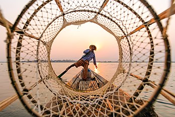 Pescador remando com a perna, visto através de sua cesta cônica, no lago Inle, Myanmar (definição 5 295 × 3 530)