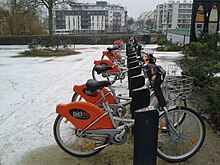 Vélos orange alignés, petite couche de neige blanche qui recouvre le sol.