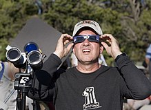 Mężczyzna ogląda zaćmienie przez okulary ze specjalnym filtrem; podobne filtry znajdują się na jego lornetce