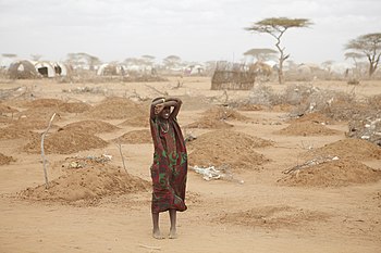 فتاةٌ صغيرةٌ تقف على أطرف مُخيِّم للاجئين وسط قُبور 70 طفلًا قضوا نحبهم نتيجة سوء التغذية، في بلدة داداب بتنزانيا، خِلال موجة القحط في أفريقيا الشرقيَّة سنة 2011م