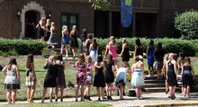 Several dozen college women in casual dresses line up on the stairs leading to an Alpha Xi Delta sorority house
