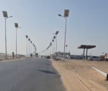 Asphaltierte Straße, gesäumt von Solarstraßenlaternen in einer Wüstengegend; einzelne flache Gebäude neben der Straße.