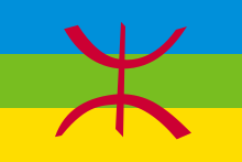 Drapeau formé de 3 bandes horizontales bleue, verte et jaune, du haut vers le bas, avec au centre une lettre rouge de l'alphabet berbère.