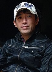 Uma fotografia de um homem japonês que veste um boné de beisebol.