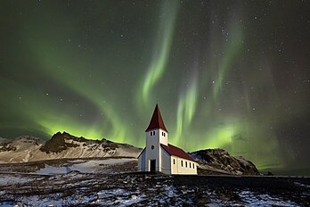 Aurora boreal sobre a igreja Víkurkirkja em Vík í Mýrdal, Islândia. Ela é uma exibição de luz natural no céu da Terra, predominantemente vista em regiões de alta latitude (ao redor do Ártico e da Antártida). As auroras exibem padrões dinâmicos de luzes brilhantes que aparecem como cortinas, raios, espirais ou cintilações dinâmicas cobrindo todo o céu. Elas são o resultado de distúrbios na magnetosfera causados ​​pelo vento solar. (definição 5 472 × 3 648)