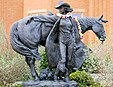 Lebensgroße Bronzeskulptur eines Cowgirls mit Westernhut und offenem Stabmantel, die sich mit dem Rücken an ihr hinter ihr stehendes Pferd lehnt