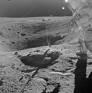 Янг готовится молотком отколоть кусок от валуна на краю кратера Плам