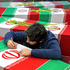 An Iranian man writes on a national flag covering a coffin of an unknown soldier who was killed during the 1980-88 Iran-Iraq war, whose remains have recently recovered from battlefields. Photo / AP