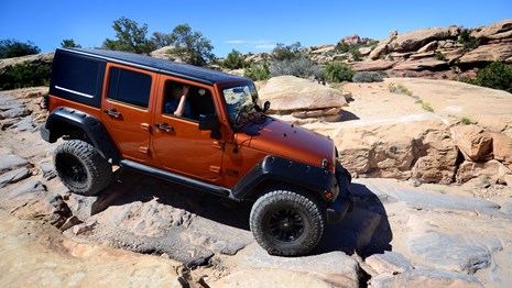 an orange Jeep driving on rocky terrain