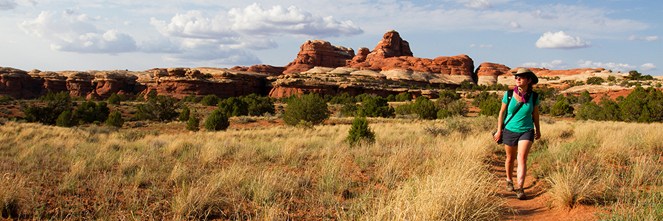 A woman hikes on a trail in front of red and white sandstone formations.