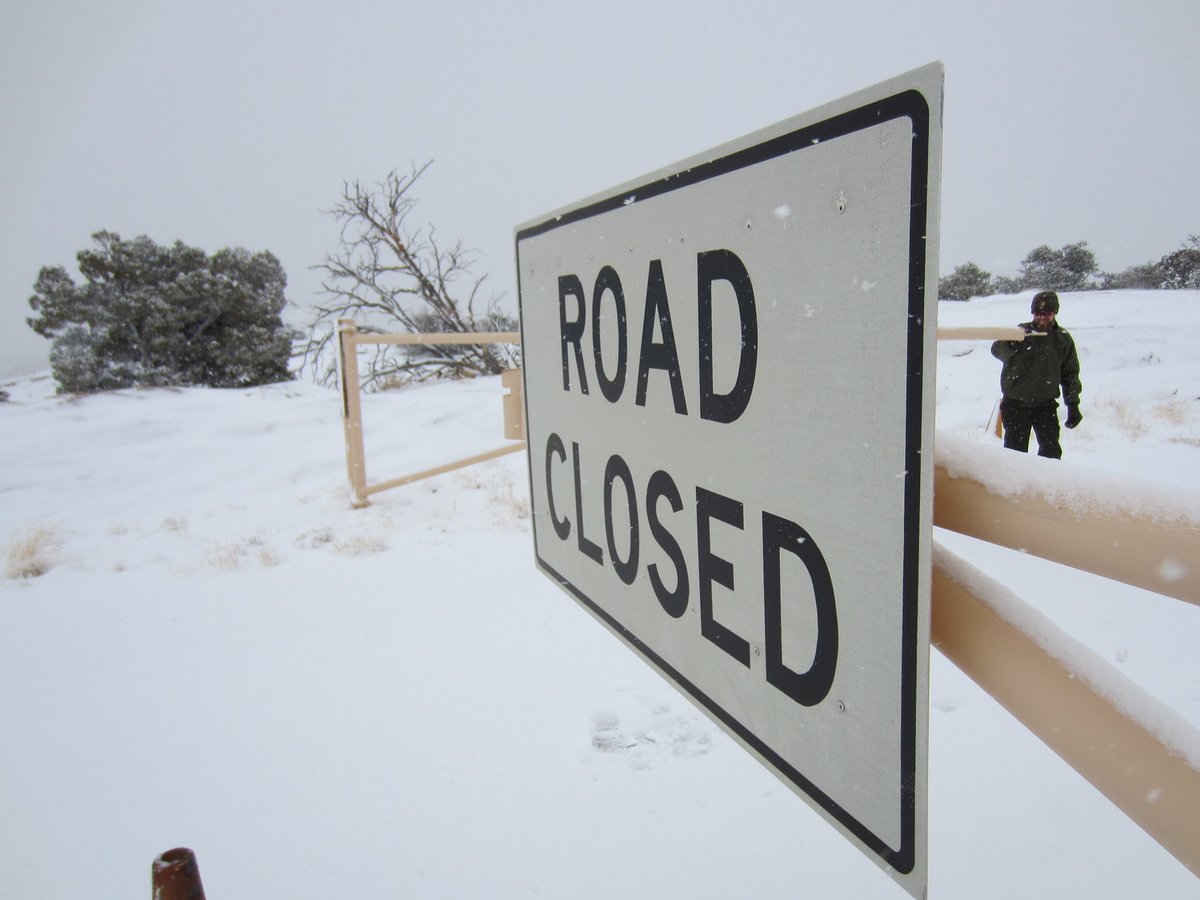 A ranger closes the gate to a snowy road, affixed with a sign that says "Road Closed."