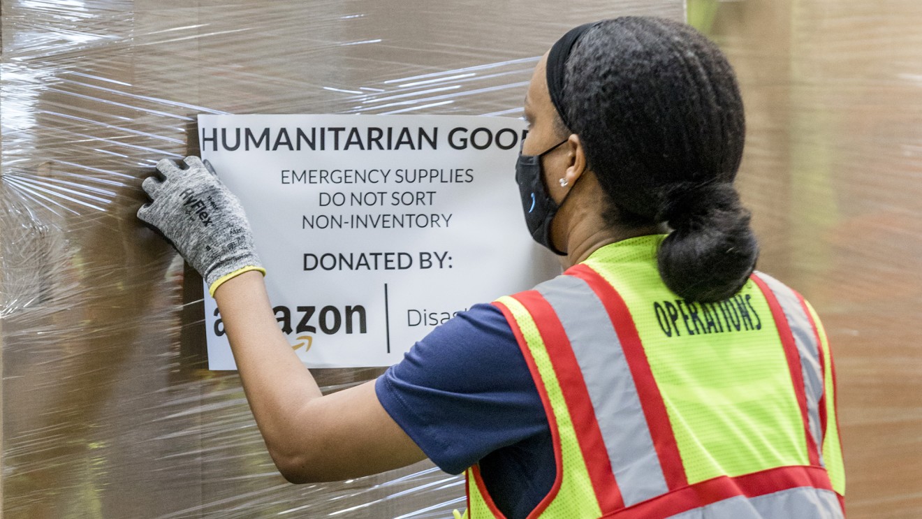 A woman wearing a mask navigates a pallet of humanitarian goods in an Amazon fulfillment center