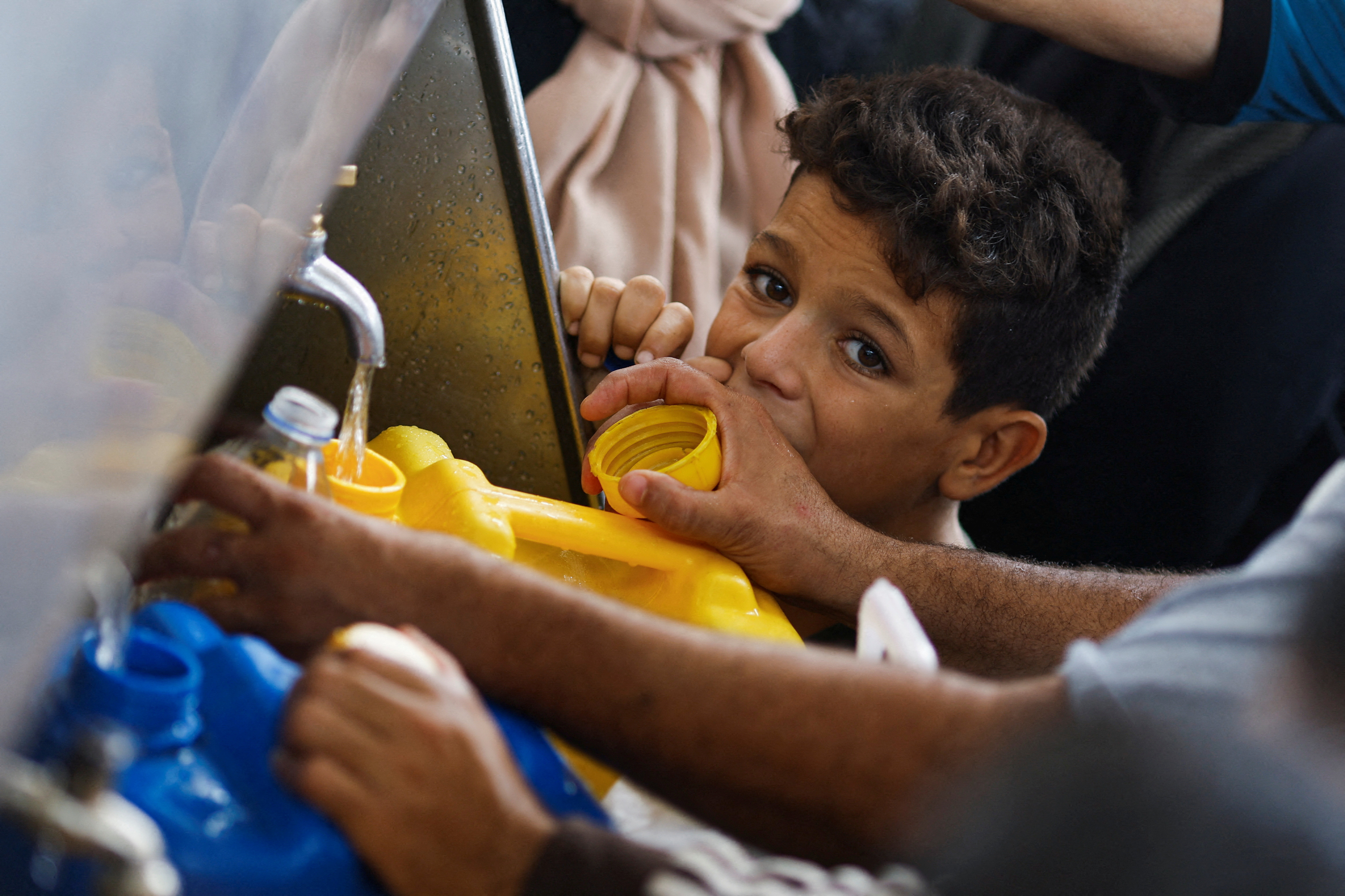 A child looks on as Palestinians gather to collect water amid water shortages, in Khan Younis