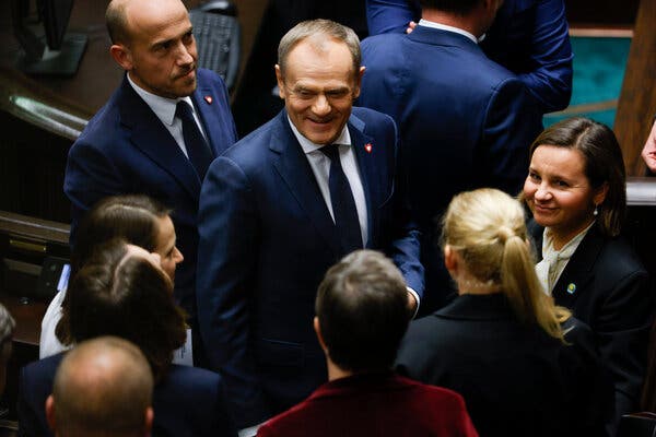 Donald Tusk, in a dark suit and tie, smiling in a crowd of people.
